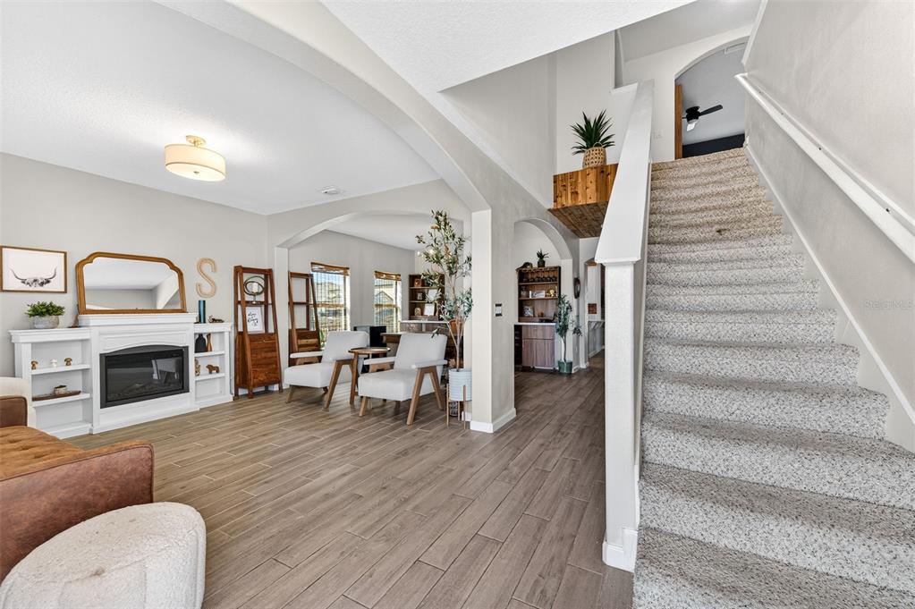 A living room features a fireplace, wood-look tile flooring, and a staircase with carpeted steps — 340 WIREGRASS AVENUE, MELBOURNE, FL