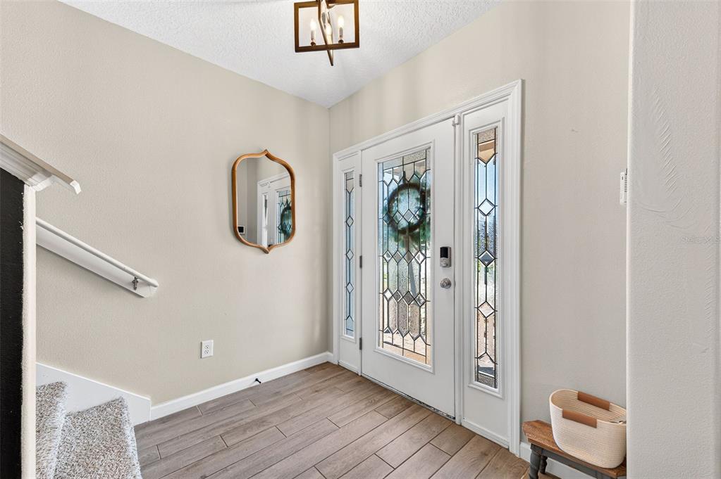 An entryway features wood-look tile flooring, a staircase, a front door with glass, and a mirror — 340 WIREGRASS AVENUE, MELBOURNE, FL