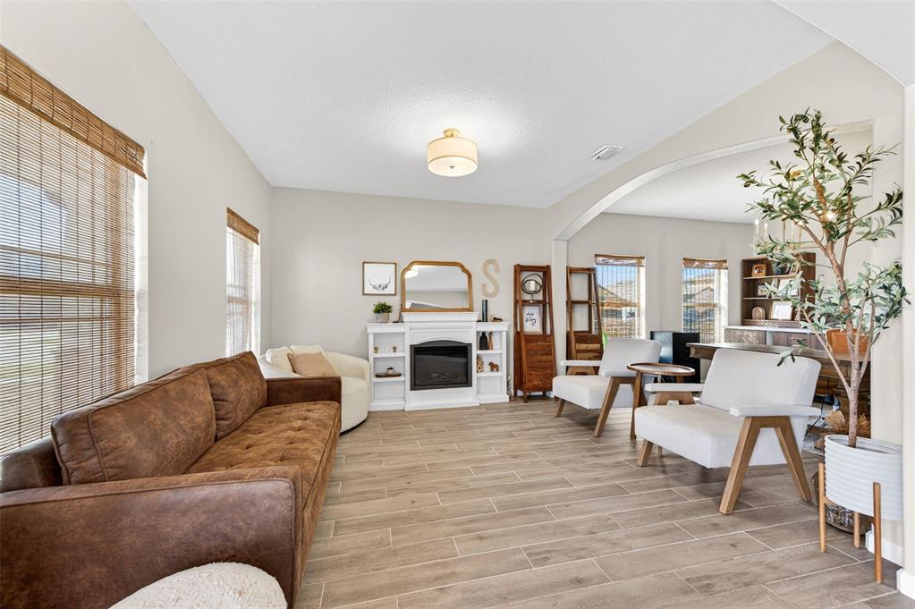 A living room features a brown sofa, white armchairs, a fireplace, and wood-look tile flooring — 340 WIREGRASS AVENUE, MELBOURNE, FL