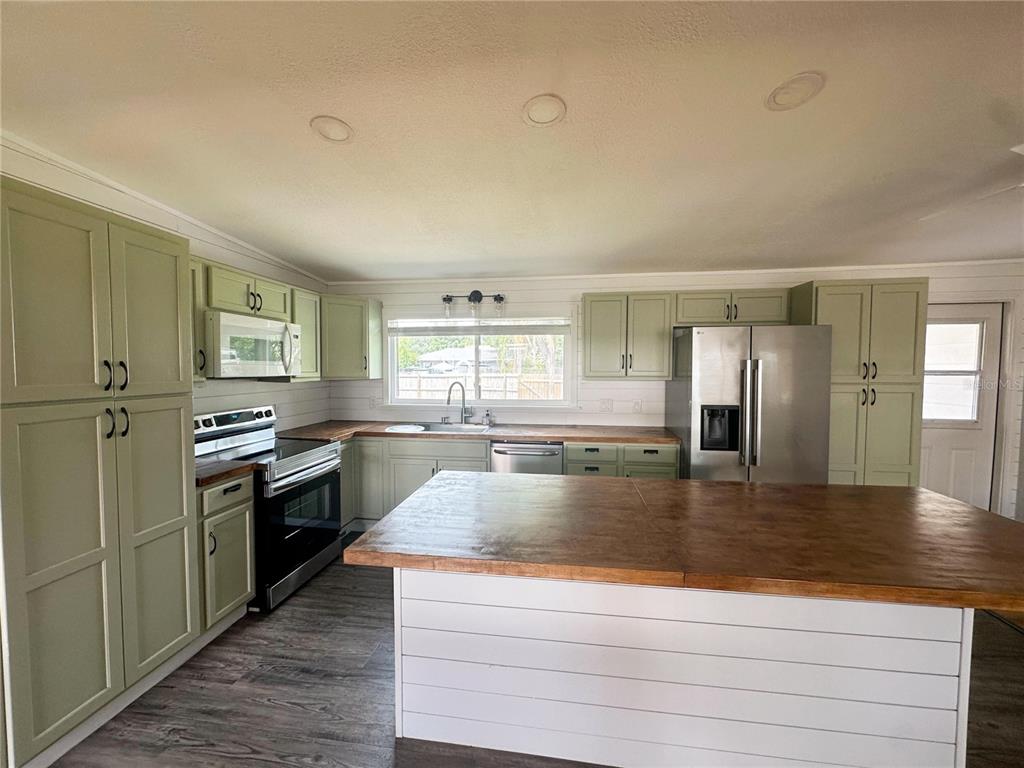 A kitchen features sage green cabinets, a large wooden island, and stainless steel appliances — 4722 HARRIS AVENUE, SARASOTA, FL