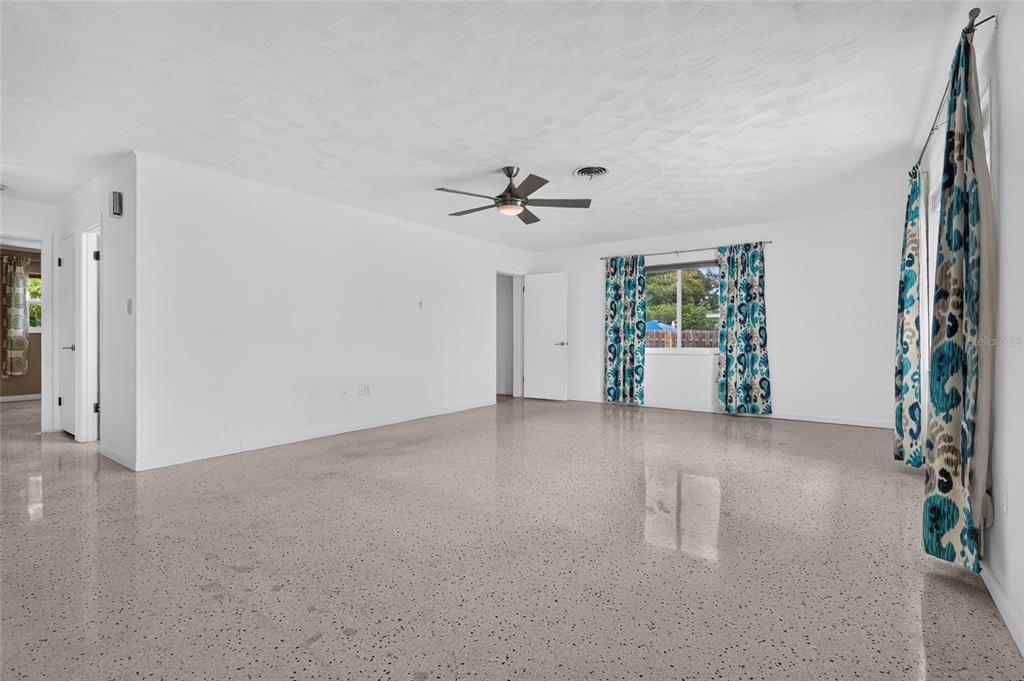 A spacious, empty living room features white walls, a ceiling fan, and speckled terrazzo flooring — 2709 MARLETTE STREET, SARASOTA, FL
