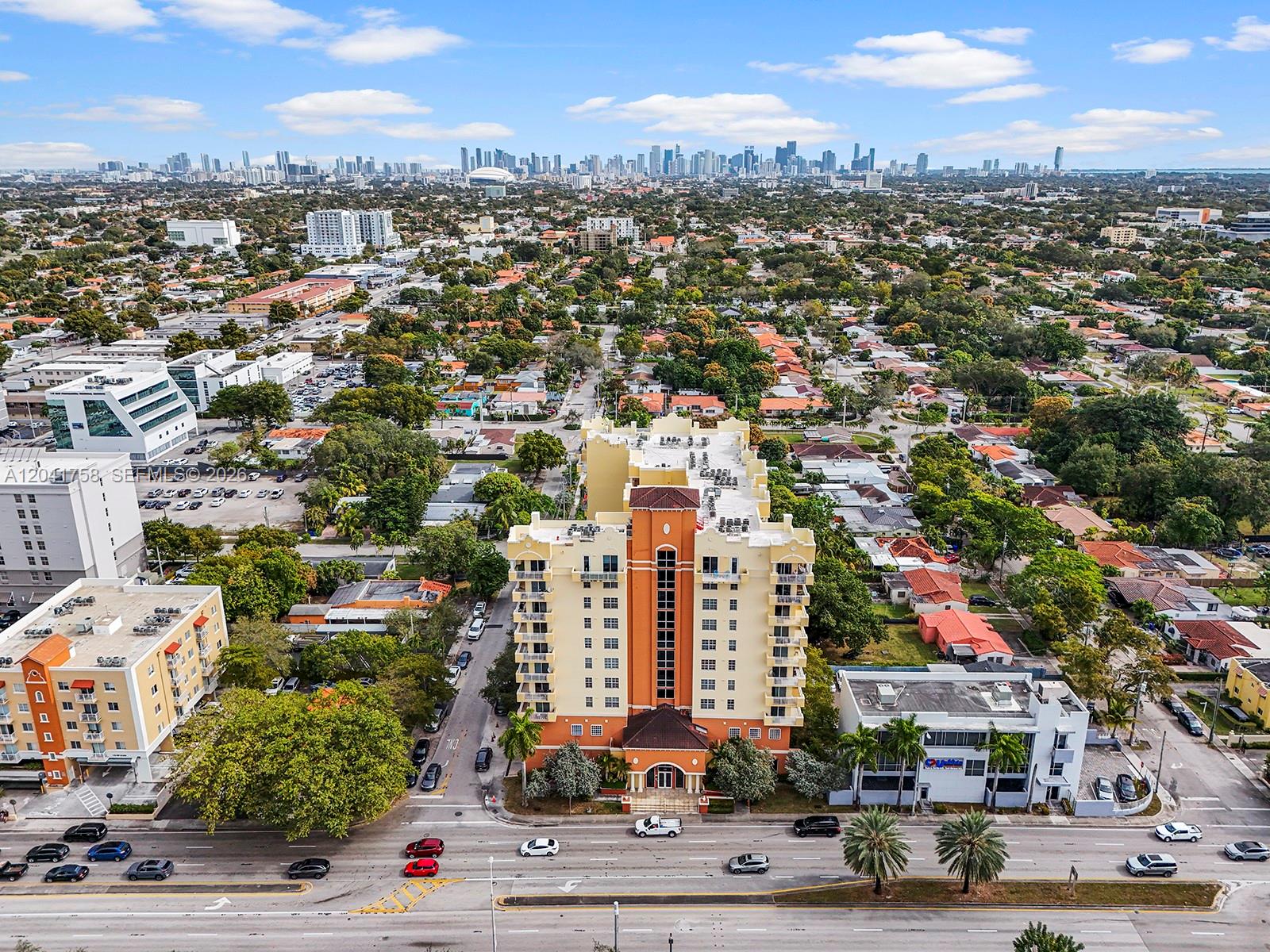 An aerial view shows a multi-story apartment building surrounded by suburban homes and city skyline — 215 SW 42nd Ave # 810, Miami FL 33134, MIAMI, FL