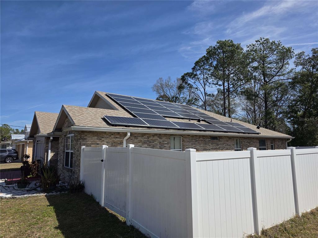 A single-story brick house features a large solar panel array installed on its roof — 34 PRAVER LANE, PALM COAST, FL