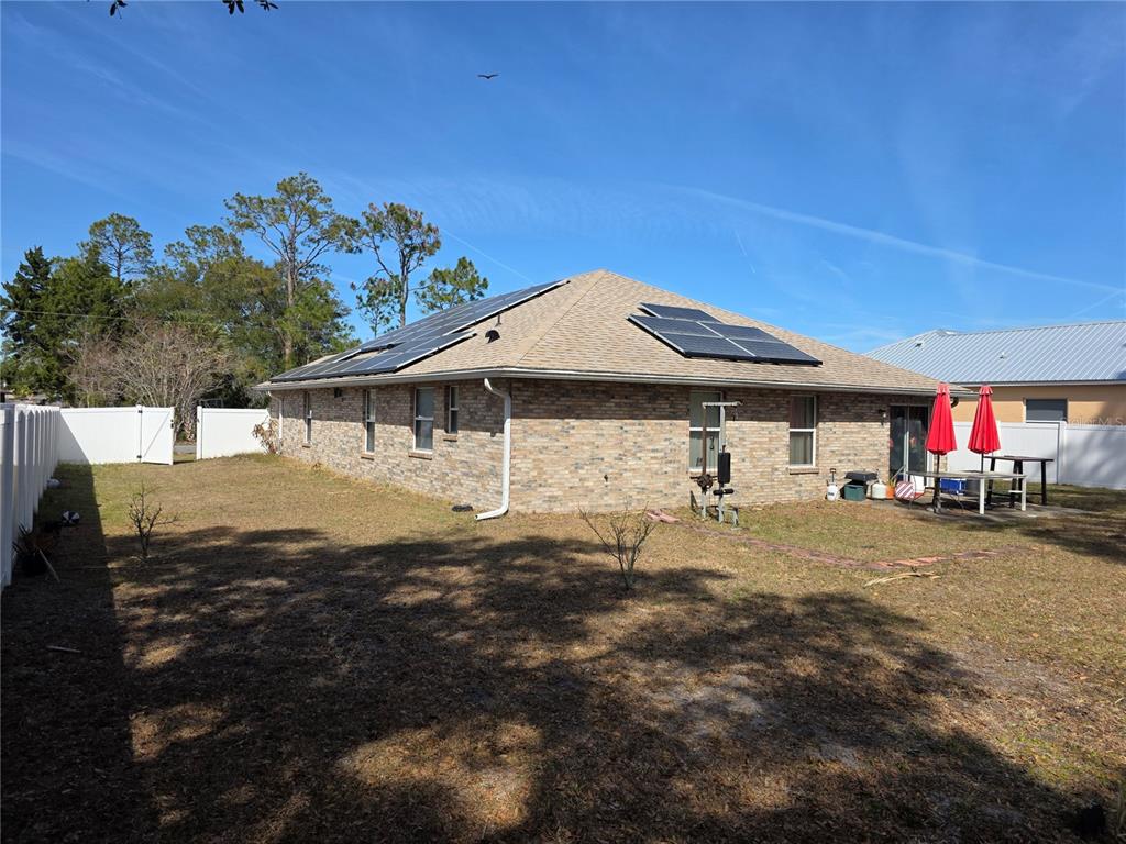 A brick house with solar panels on the roof sits in a fenced backyard — 34 PRAVER LANE, PALM COAST, FL