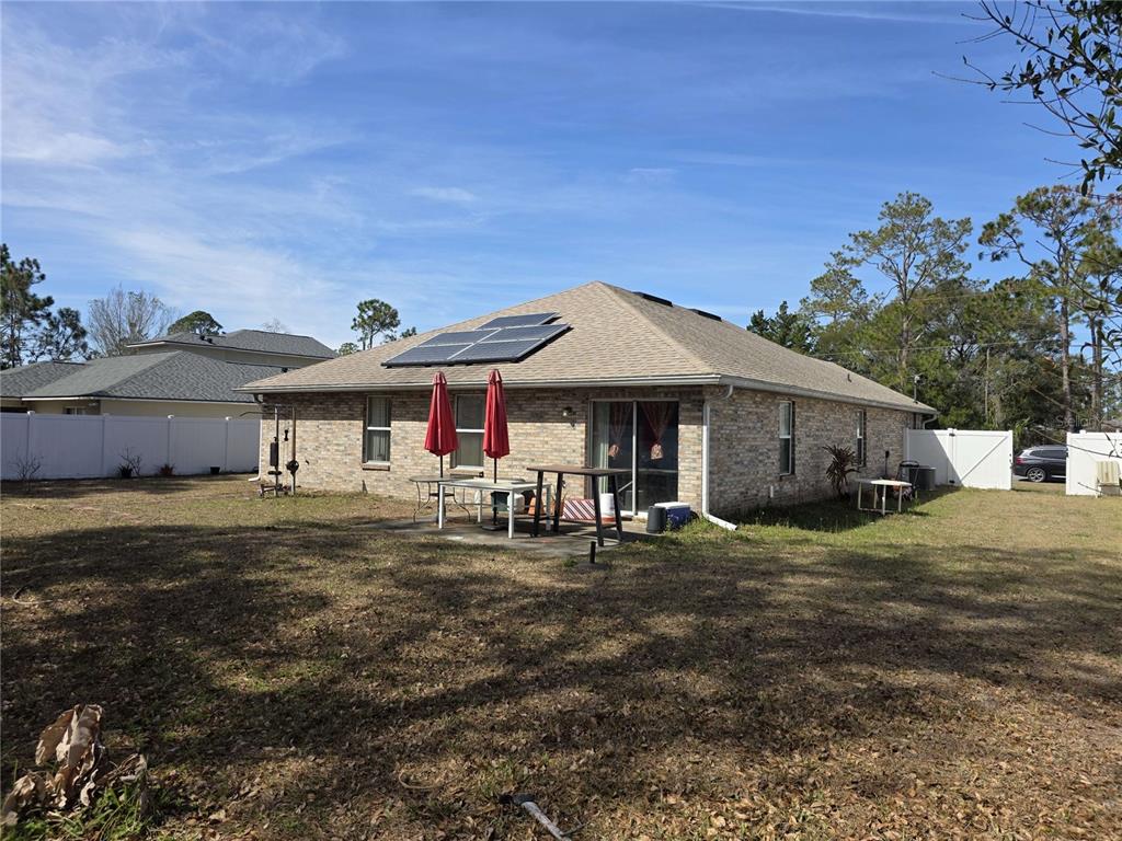 The rear exterior of a brick house features a patio, solar panels, and a yard — 34 PRAVER LANE, PALM COAST, FL