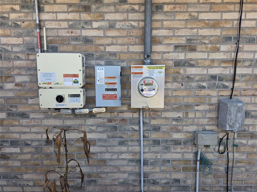 An exterior brick wall features a solar power inverter, disconnect switch, and utility electric meter — 34 PRAVER LANE, PALM COAST, FL