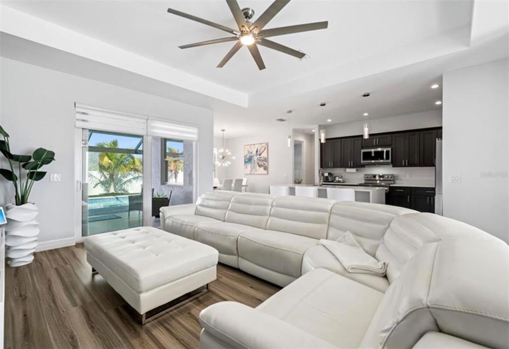 A modern living room with a white sectional sofa, ottoman, and an open-concept kitchen — 1017 NW 15TH TERRACE, CAPE CORAL, FL