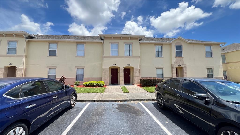 A two-story apartment building exterior with two front doors and parked cars in the foreground — 2848 CLUB CORTILE CIRCLE, KISSIMMEE, FL