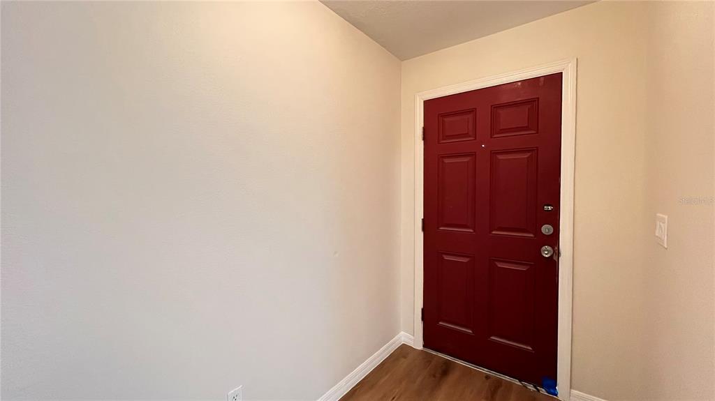 An interior entryway features a red front door, light-colored walls, and wood-look flooring — 2848 CLUB CORTILE CIRCLE, KISSIMMEE, FL