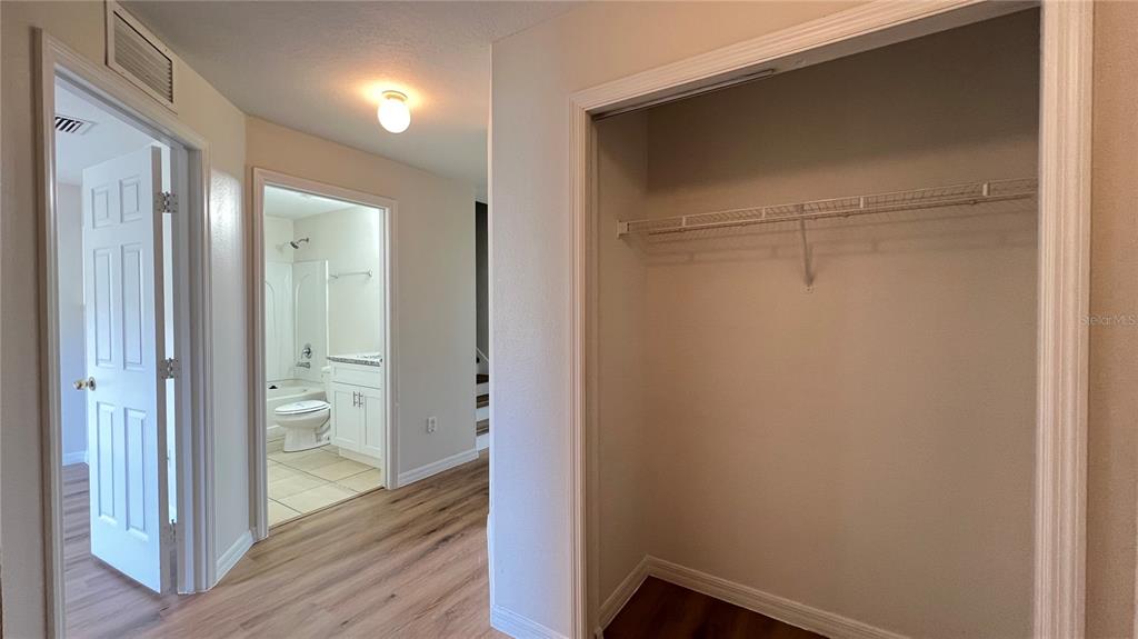 A hallway features a closet with wire shelving, a bathroom doorway, and light wood flooring — 2848 CLUB CORTILE CIRCLE, KISSIMMEE, FL
