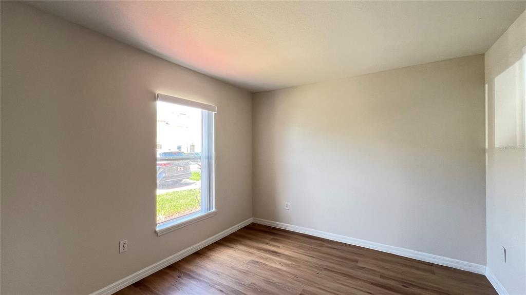An empty room features light-colored walls, wood-look flooring, and a single window with a blind — 2848 CLUB CORTILE CIRCLE, KISSIMMEE, FL