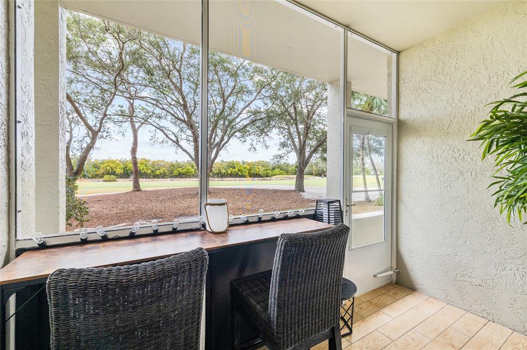 A screened-in porch features a wooden bar table with two chairs overlooking a golf course — 2333 FEATHER SOUND DRIVE UNIT A101, CLEARWATER, FL