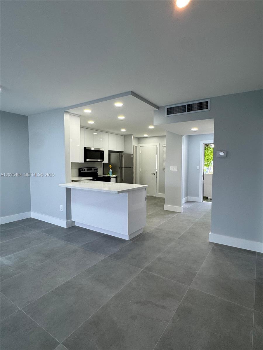 A modern kitchen with white cabinets and a breakfast bar opens to a living area — 1680 NE 191st St # 2, Miami FL 33179, MIAMI, FL