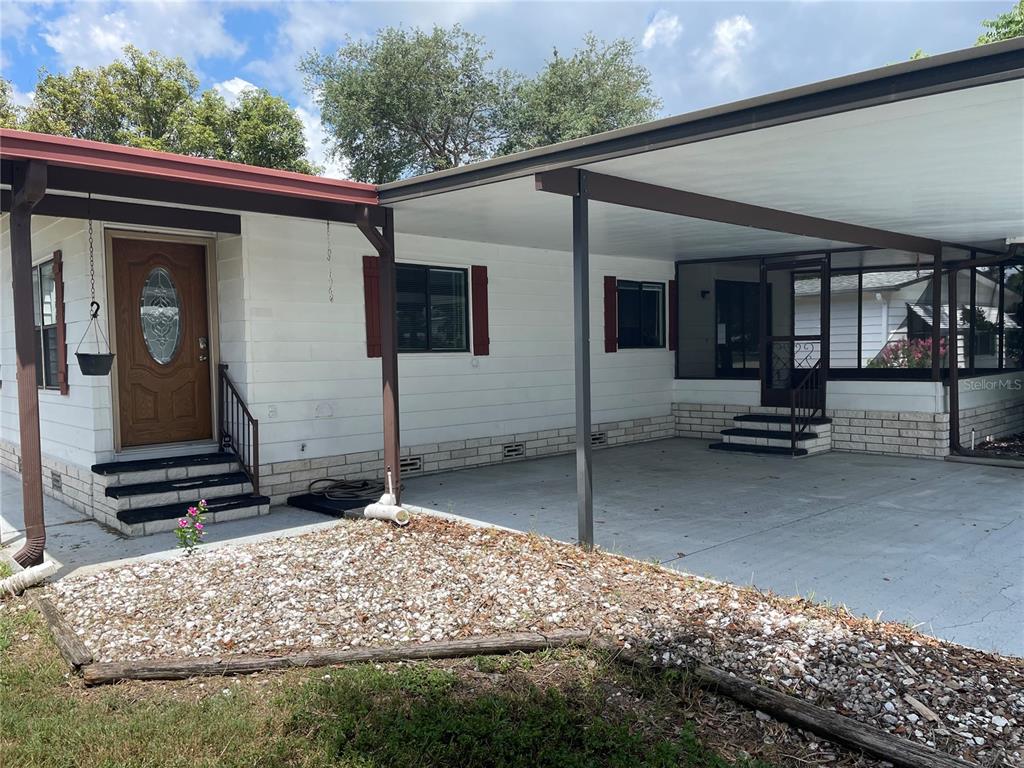 A mobile home exterior features a white facade, red shutters, a carport, and a screened porch — 2102 CANOPY CIRCLE UNIT 150, ZELLWOOD, FL