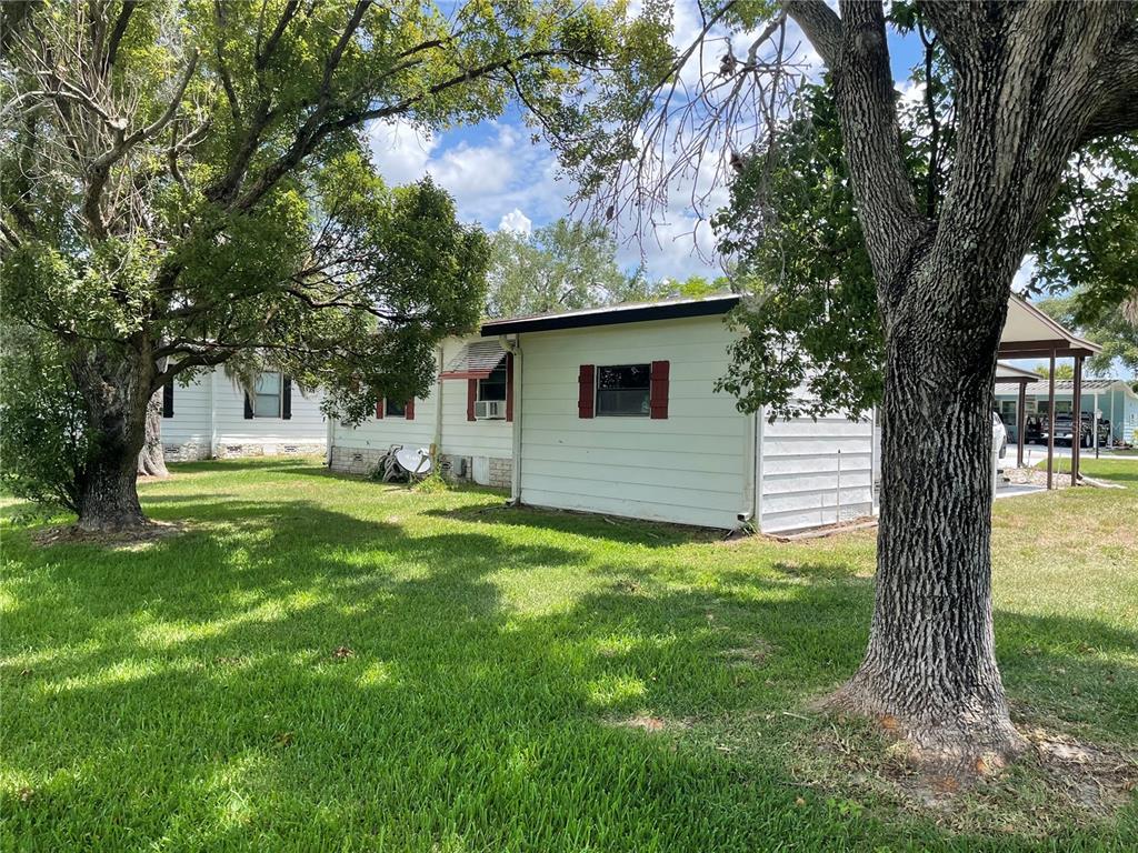 A white house with red shutters sits on a grassy lot shaded by large trees — 2102 CANOPY CIRCLE UNIT 150, ZELLWOOD, FL