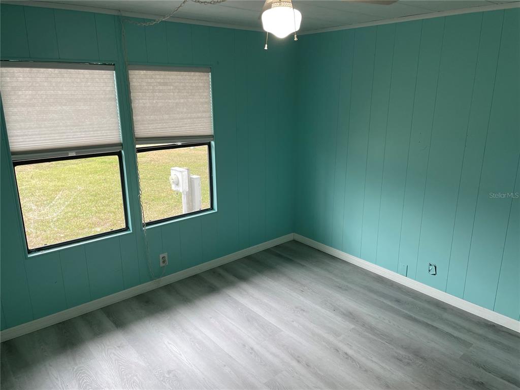 An empty room features teal wood-paneled walls, light gray wood-look flooring, and two windows — 2102 CANOPY CIRCLE UNIT 150, ZELLWOOD, FL