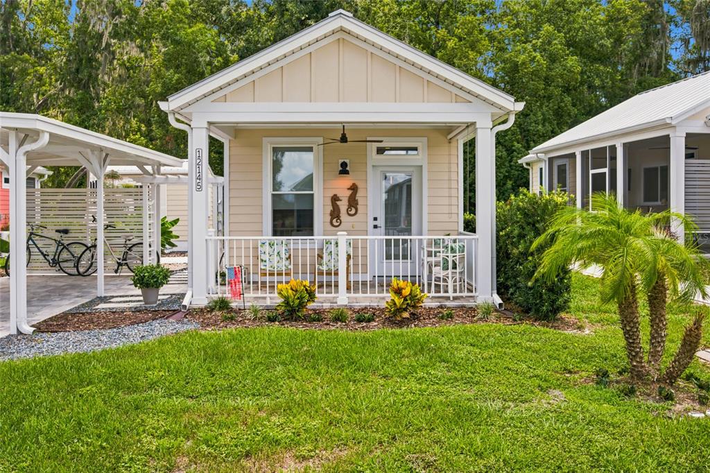 A small, light-colored cottage with a front porch, white railing, and a covered carport — 12145 GRAND OAK LANE, OXFORD, FL