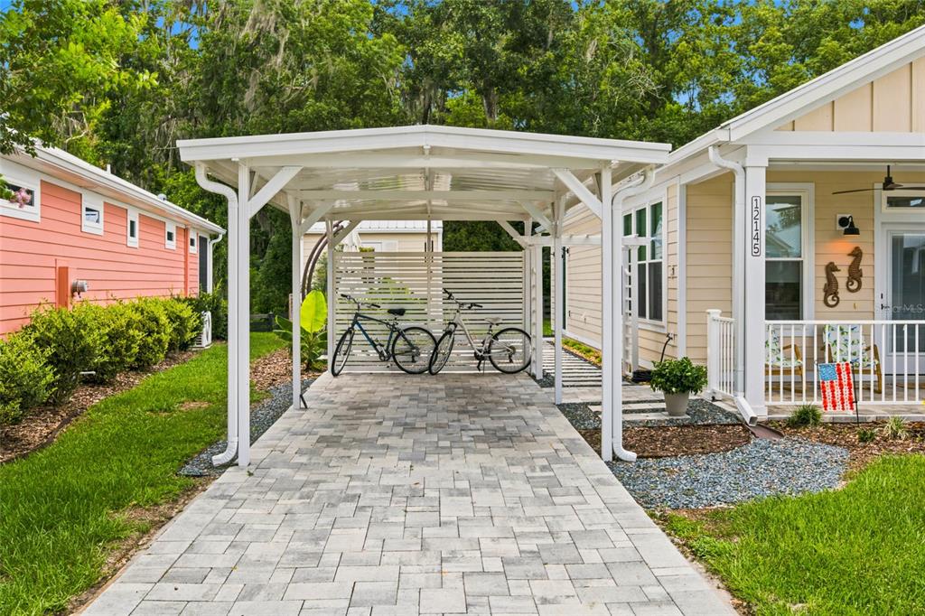 A paved carport with two bicycles sits between a peach house and a yellow house — 12145 GRAND OAK LANE, OXFORD, FL