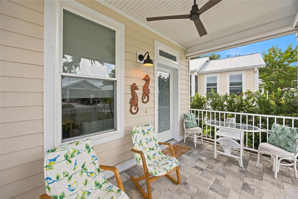 A covered porch features a paver floor, outdoor seating, and seahorse wall decor — 12145 GRAND OAK LANE, OXFORD, FL