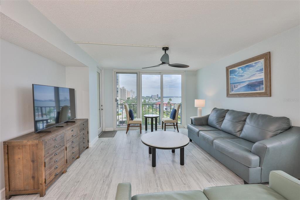 A living room features a grey leather sofa, a wooden media console, and balcony views — 1400 GULF BOULEVARD UNIT 704, CLEARWATER BEACH, FL