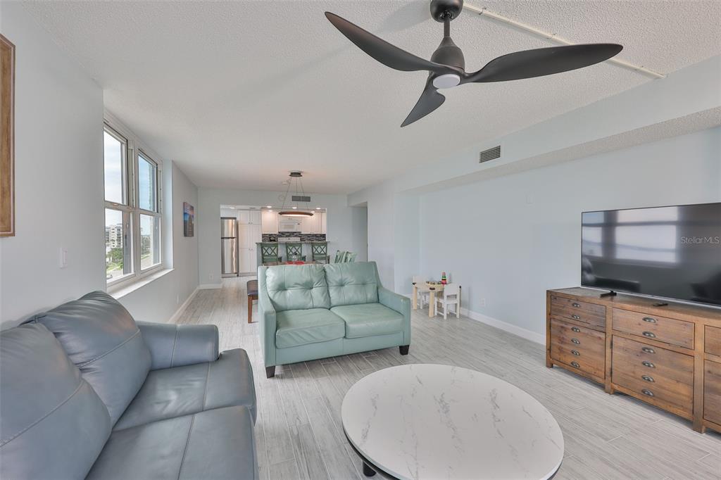 A living room features light wood-look flooring, a ceiling fan, and a view into the kitchen — 1400 GULF BOULEVARD UNIT 704, CLEARWATER BEACH, FL