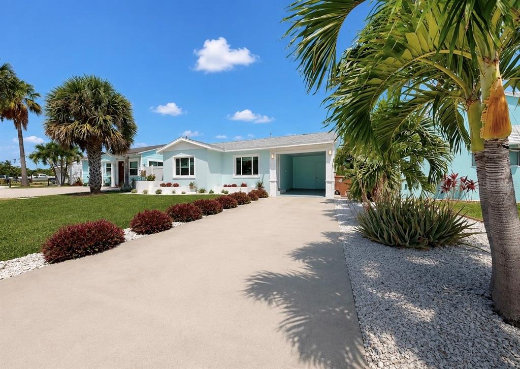 A light blue single-story house features a concrete driveway, palm trees, and landscaped garden beds — 480 S BAYSHORE DRIVE, MADEIRA BEACH, FL