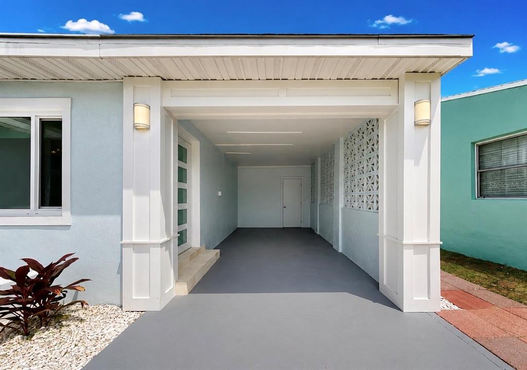 A covered carport with white columns, a light blue exterior, and a decorative breeze block wall — 480 S BAYSHORE DRIVE, MADEIRA BEACH, FL