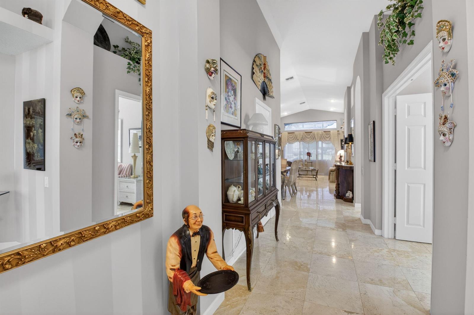 A tiled hallway features a decorative butler statue, a curio cabinet, and wall-mounted Venetian masks — 11550 Ballylee Terrace, Boynton Beach FL 33437, BOYNTON BEACH, FL
