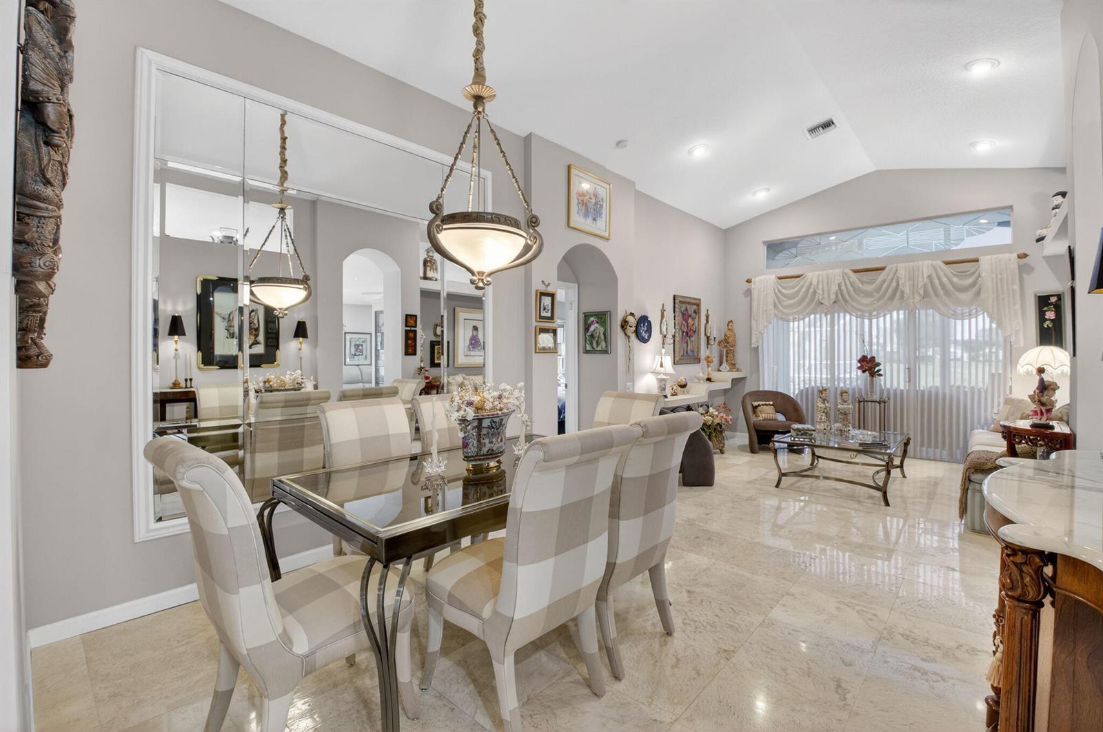 A dining area with a glass table and plaid chairs sits before a large wall mirror — 11550 Ballylee Terrace, Boynton Beach FL 33437, BOYNTON BEACH, FL