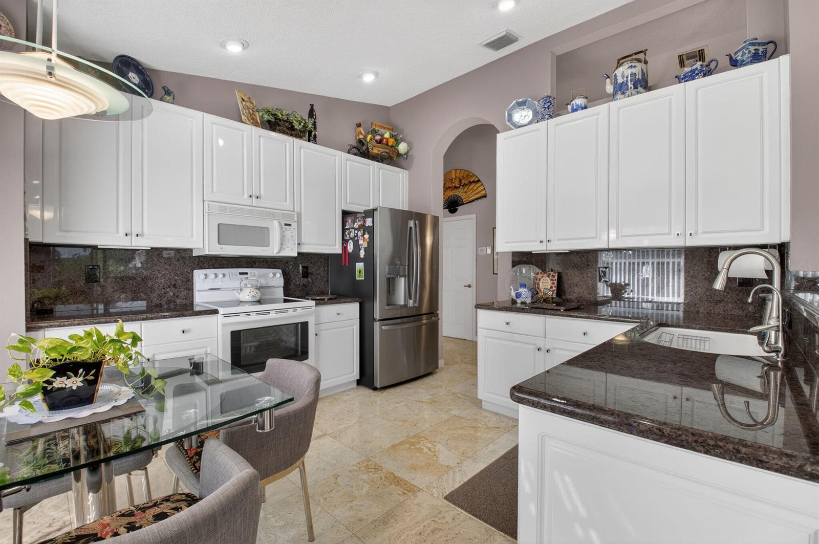 A kitchen features white cabinetry, dark granite countertops, stainless steel appliances, and a glass dining table — 11550 Ballylee Terrace, Boynton Beach FL 33437, BOYNTON BEACH, FL