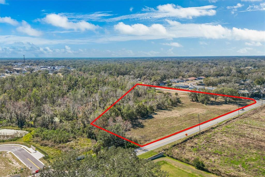 An aerial view shows a vacant, partially wooded lot outlined in red along a road — 7835 KATHLEEN ROAD, LAKELAND, FL