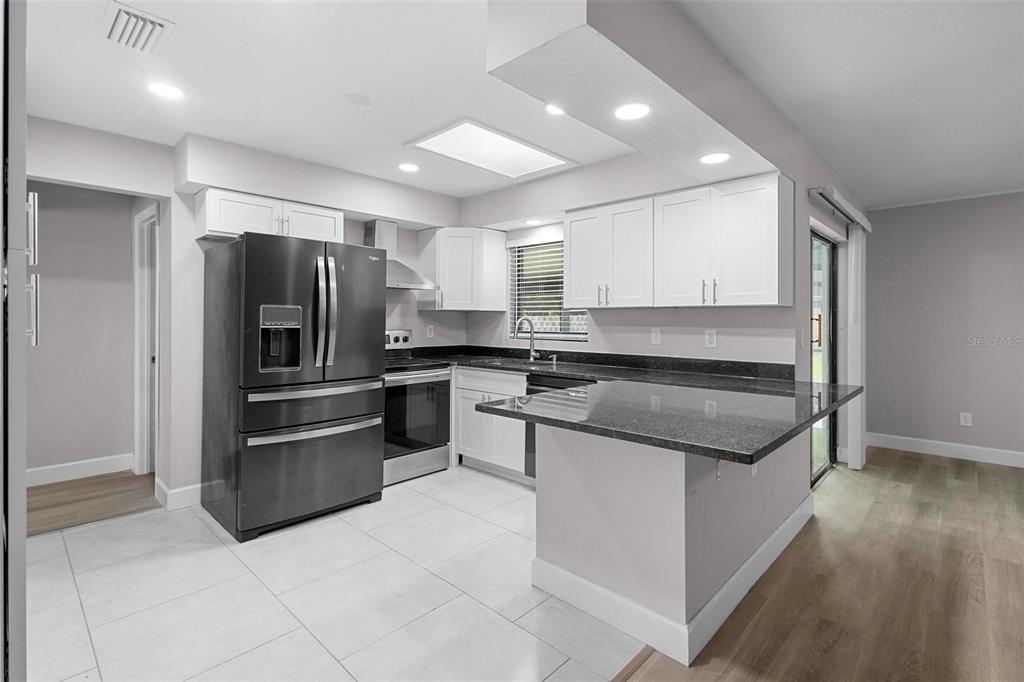 A kitchen features white cabinets, dark granite countertops, stainless steel appliances, and light tile flooring — 10140 BRIDLEWOOD AVENUE, ORLANDO, FL