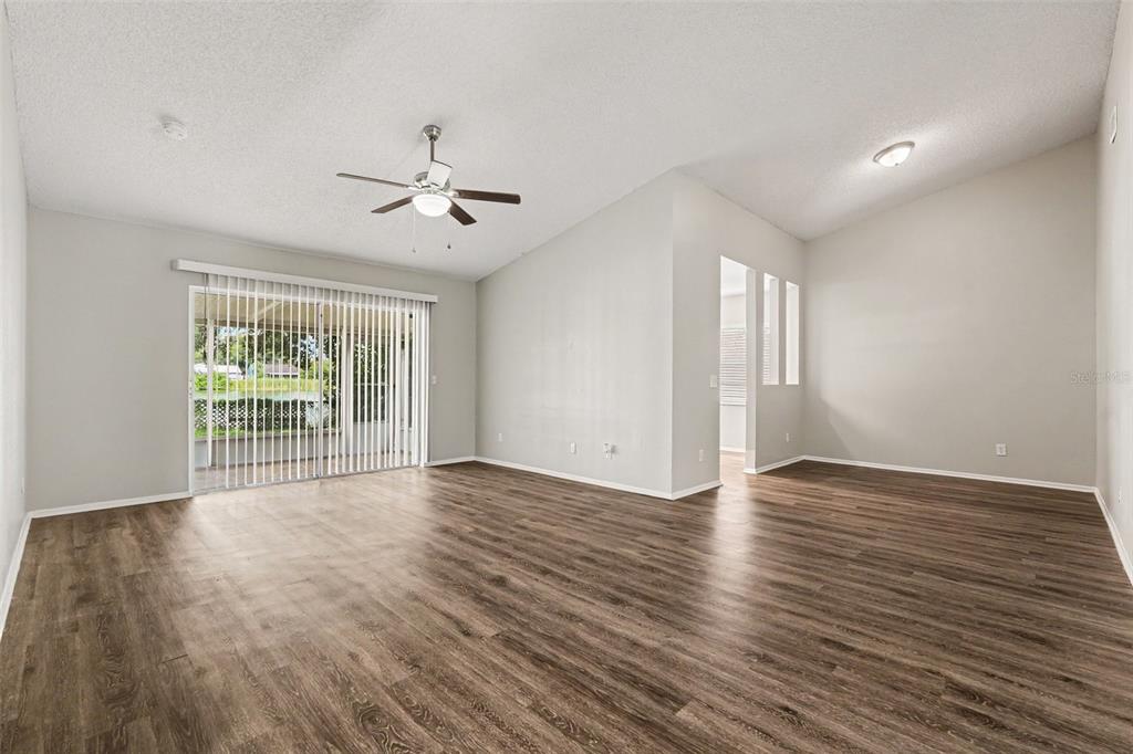 An empty living room with wood-look flooring, a ceiling fan, and sliding glass patio doors — 8304 NATCHEZ STREET, TAMPA, FL