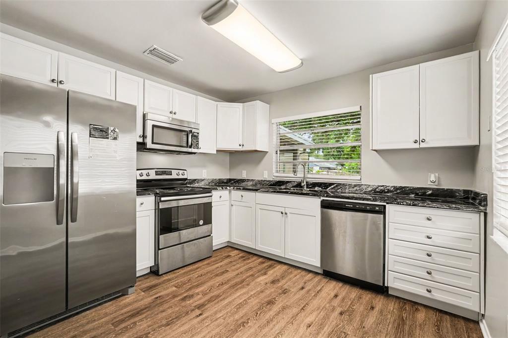 A kitchen with white cabinets, stainless steel appliances, and black granite countertops — 8304 NATCHEZ STREET, TAMPA, FL