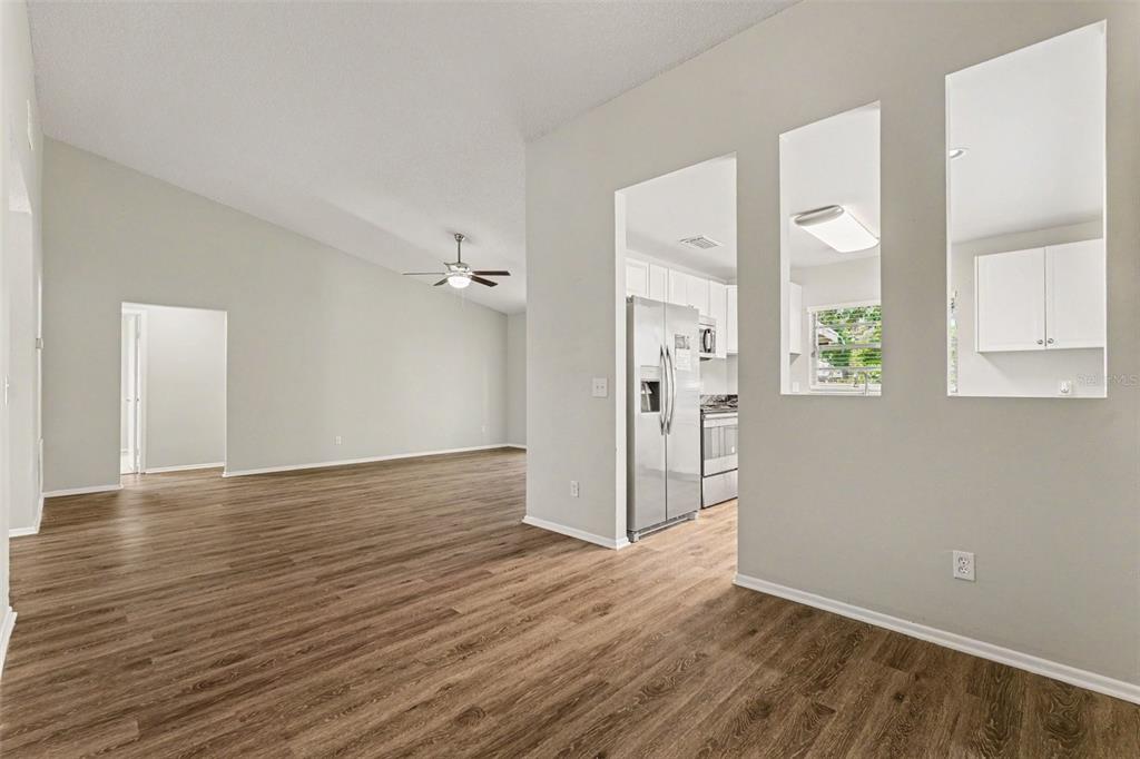 An open-concept living area features wood-look flooring, a vaulted ceiling, and a pass-through kitchen window — 8304 NATCHEZ STREET, TAMPA, FL