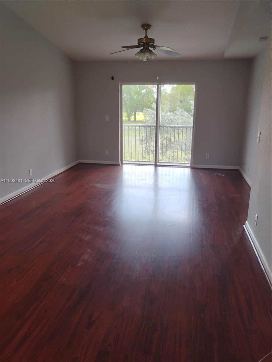 An empty room features dark wood-look flooring, light gray walls, and a sliding glass door — 3748 NW 91st Ln # 3748, Sunrise FL 33351, SUNRISE, FL