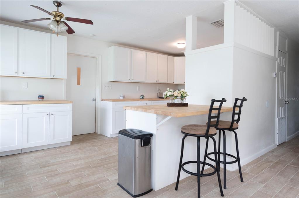 A kitchen features white cabinets, light wood countertops, a breakfast bar with two stools, and tile flooring — 4833 CROW STREET, ORLANDO, FL