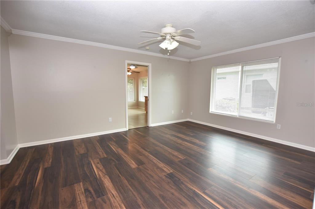 An empty room features dark wood-look flooring, light gray walls, a ceiling fan, and windows — 928 E VALENCIA STREET, LAKELAND, FL