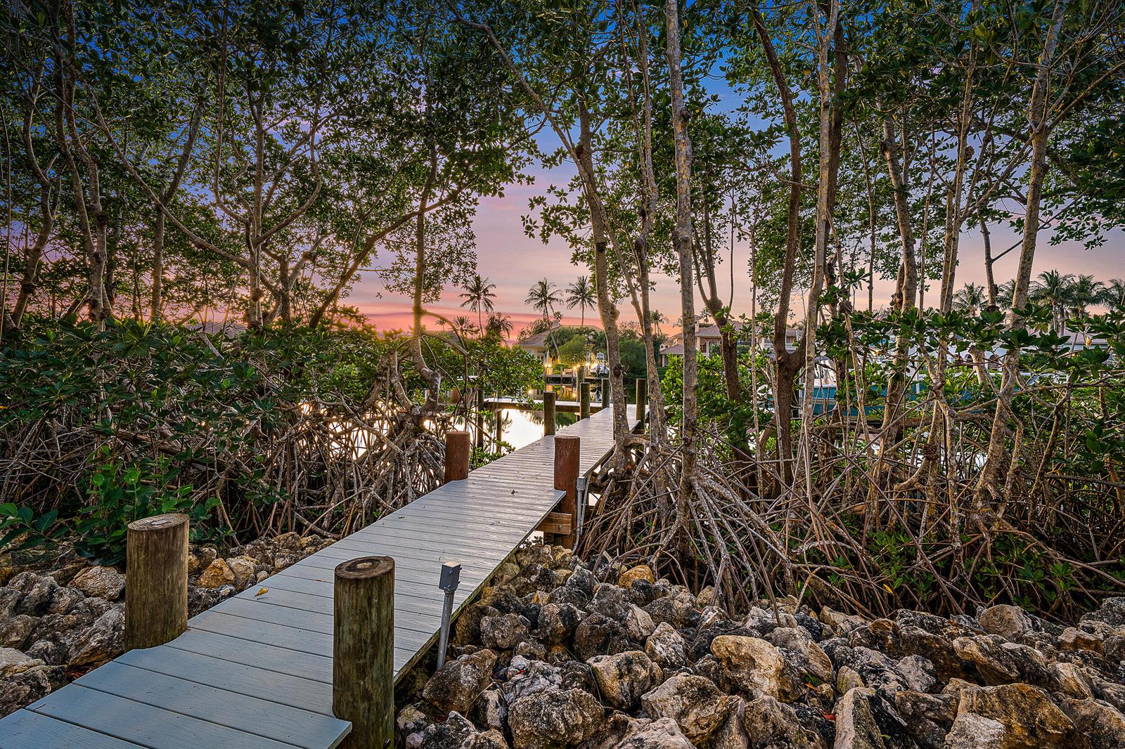 A wooden dock extends through a mangrove forest toward a canal at sunset — 9176 SE River Terrace, Jupiter FL 33469, JUPITER, FL