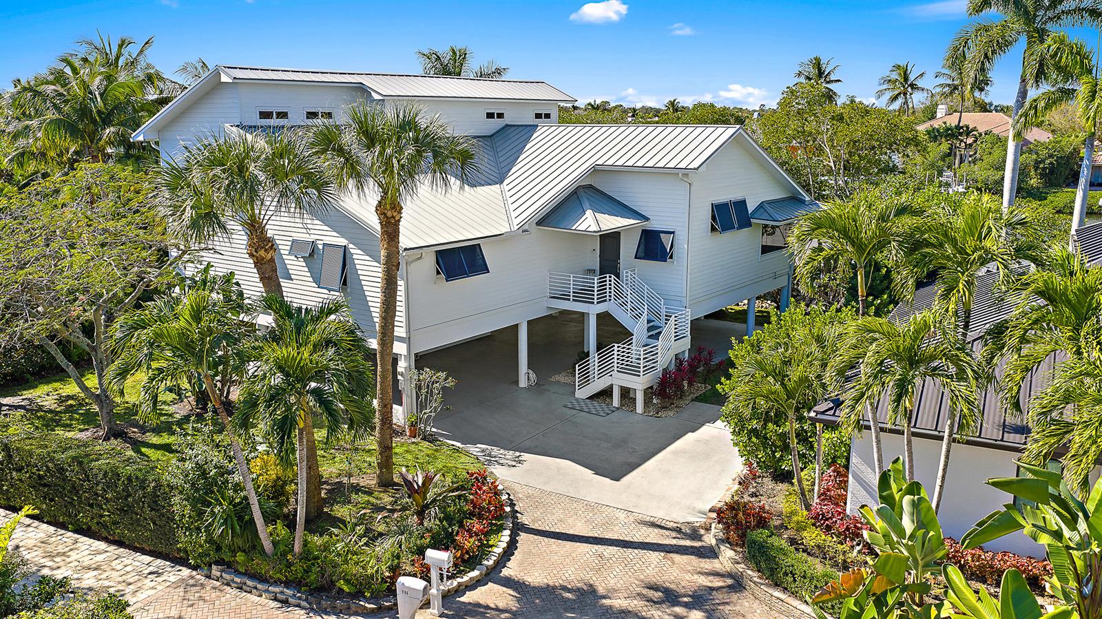 An elevated white house with a metal roof stands above a concrete driveway and landscaping — 9176 SE River Terrace, Jupiter FL 33469, JUPITER, FL
