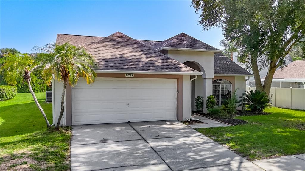 A single-story house with a white garage door, tan stucco walls, and a shingled roof — 9718 PLEASANT RUN WAY, TAMPA, FL