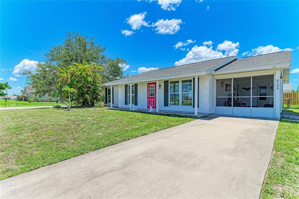 A single-story white brick house with a red front door and a screened-in front porch — 6195 LA PORTE TERRACE, PORT CHARLOTTE, FL