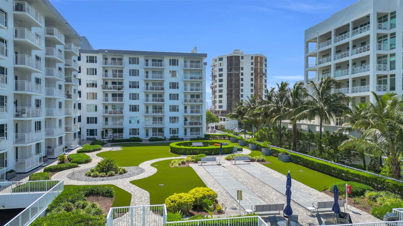 An elevated view of a landscaped courtyard with shuffleboard courts between two white apartment buildings — 3114 S Ocean Boulevard # 705, Highland Beach FL 33487, HIGHLAND BEACH, FL