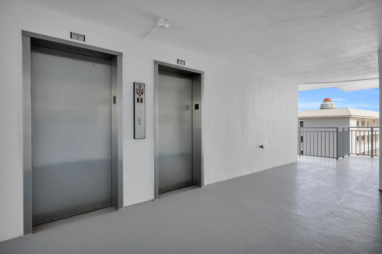 Two stainless steel elevators are set into a white wall on a gray concrete balcony — 3114 S Ocean Boulevard # 705, Highland Beach FL 33487, HIGHLAND BEACH, FL