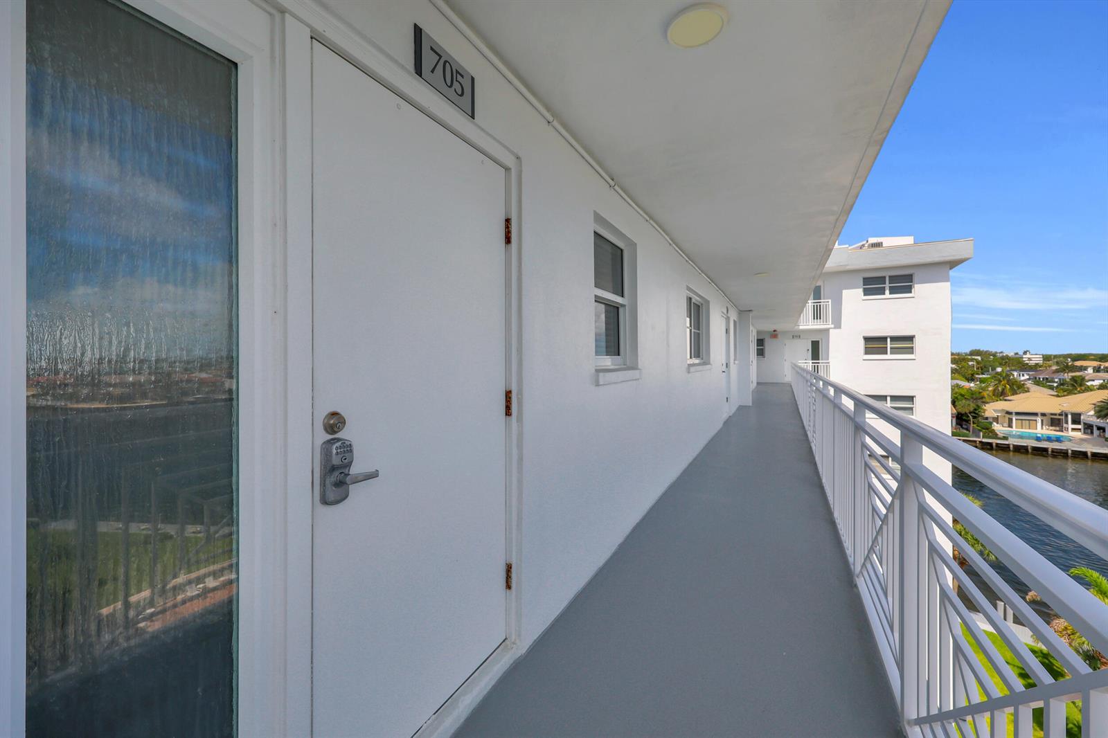 An outdoor apartment building walkway features white doors, a keypad lock, and a metal railing — 3114 S Ocean Boulevard # 705, Highland Beach FL 33487, HIGHLAND BEACH, FL