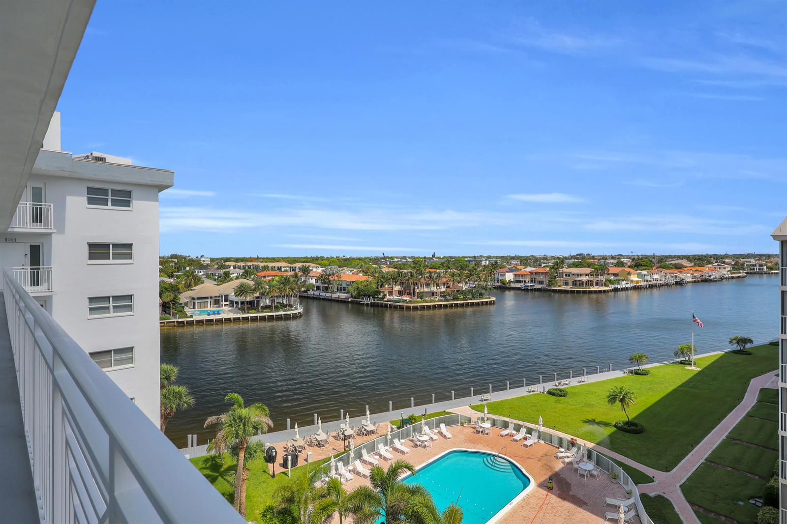 An elevated view of a swimming pool, lawn, and waterway surrounded by residential buildings — 3114 S Ocean Boulevard # 705, Highland Beach FL 33487, HIGHLAND BEACH, FL