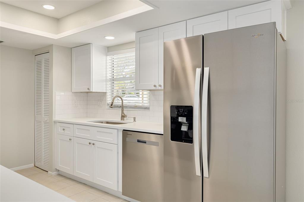 A bright kitchen features white cabinets, stainless steel appliances, white countertops, and light tile flooring — 3569 OAK LAKE DRIVE, PALM HARBOR, FL