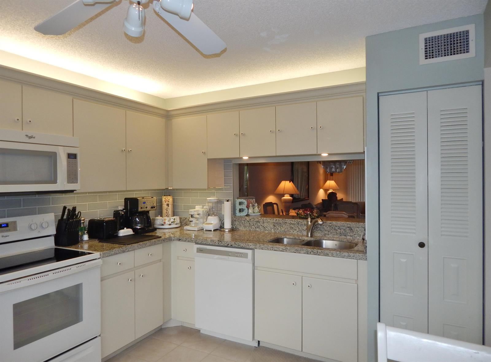 A kitchen features white cabinets, granite countertops, a double sink, and a white appliance suite — 6698 N 10th Ave N # 215, Lake Worth FL 33467, LAKE WORTH, FL