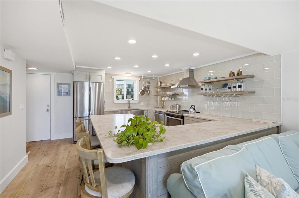 A kitchen with a stone-topped peninsula, light wood flooring, and open shelving on tiled walls — 3510 S OCEAN SHORE BOULEVARD UNIT 217, FLAGLER BEACH, FL