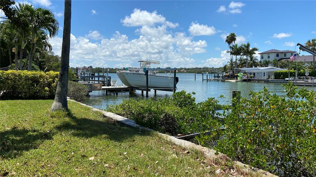 A boat sits on a lift in a canal next to a grassy waterfront yard — 321 12TH AVENUE, INDIAN ROCKS BEACH, FL